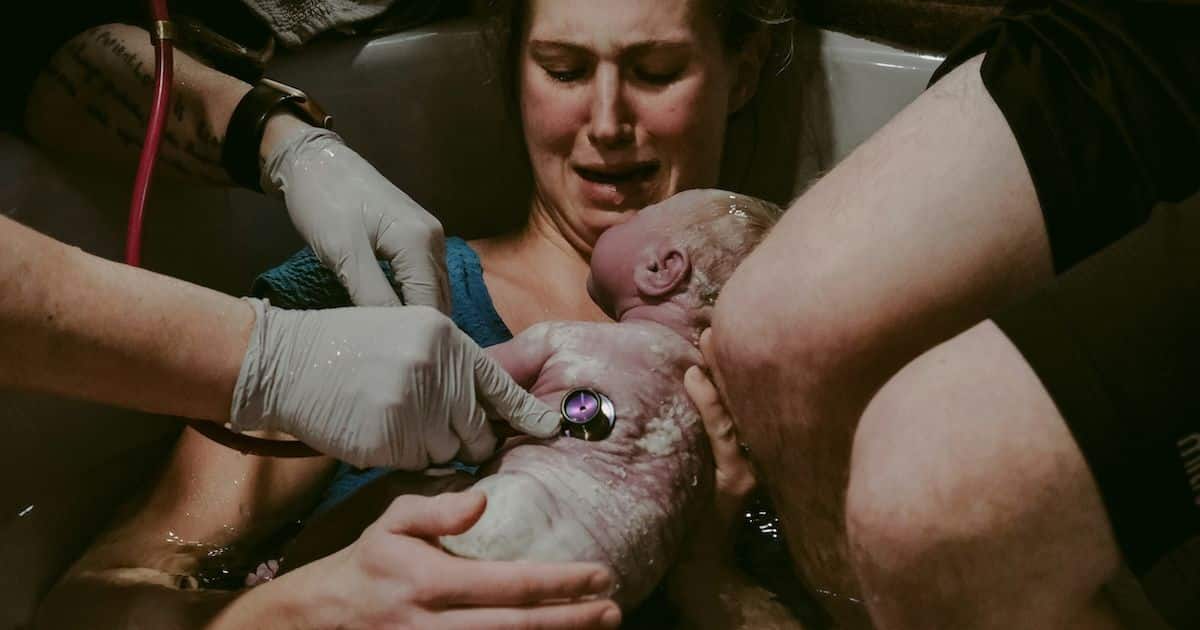 woman giving birth in tub with newborn on chest